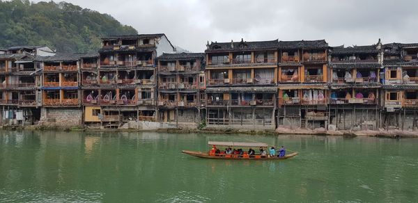 Boats in river by buildings against sky