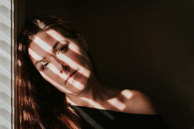 Portrait of woman beside a window with shadows across her face.