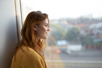 Portrait of young woman looking away while sitting on window