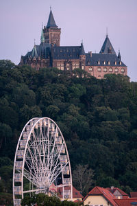 Ferris wheel by building in city against sky