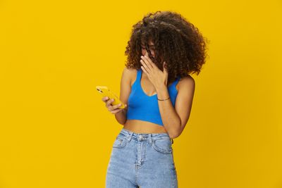 Young woman with arms raised against yellow background