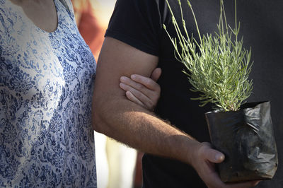 Midsection of man holding woman standing against potted plants