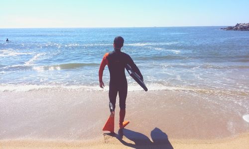 Rear view of man standing on beach against sky