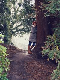 Full length of woman leaning on tree trunk