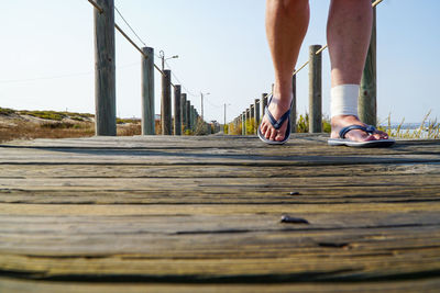 Low section of man walking on bridge against sky