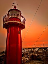 Lighthouse by sea against sky during sunset