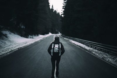 Rear view of woman with backpack walking on road during winter