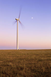 Wind turbine in motion against blue sky with moon