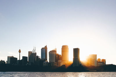 Modern cityscape by river against clear sky