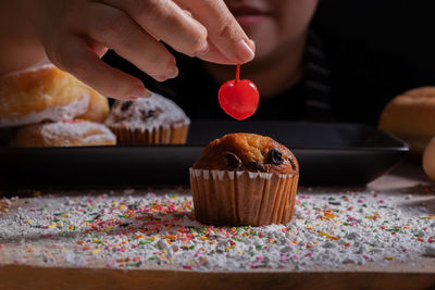 Woman holding cherry over cupcake