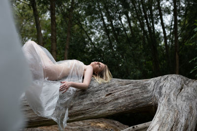 Woman lying on tree trunk in forest