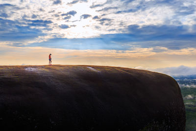 Mid distance of woman standing on mountain against cloudy sky during sunset