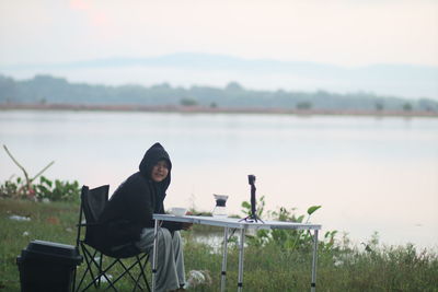 Man sitting by lake against sky