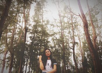 Portrait of young woman standing by trees in forest