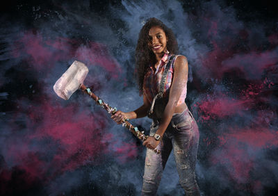 Portrait of young woman holding hammer while standing against colored background