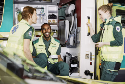 Happy multi-ethnic paramedics talking while sitting in ambulance at parking lot