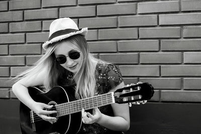 Young woman playing guitar against brick wall