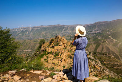 Rear view of woman standing on mountain against blue sky