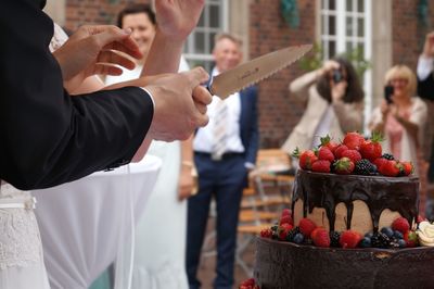 Cropped image of bride and groom cutting cake during wedding