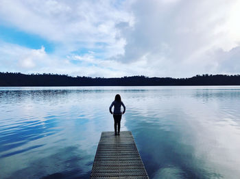 Rear view of man standing on pier over lake against sky