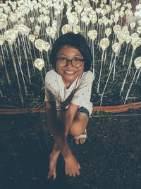 Portrait of smiling girl sitting against illuminated light bulbs