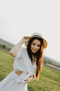 Young woman wearing hat standing on field against sky