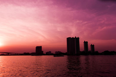 Silhouette buildings by sea against romantic sky at sunset