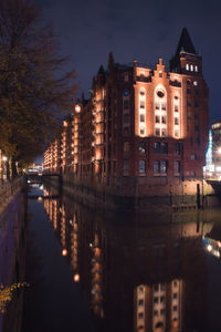 Illuminated buildings by river against sky at night