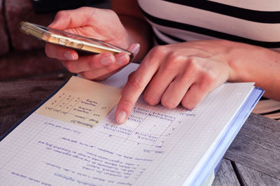 Midsection of woman studying while using smartphone on table