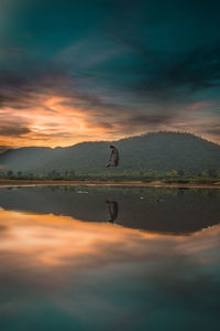 Man jumping over lake against sky during sunset