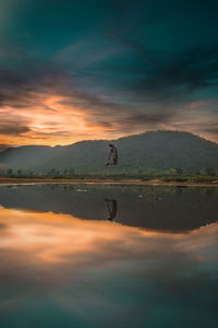 Reflection of man in lake against sky during sunset