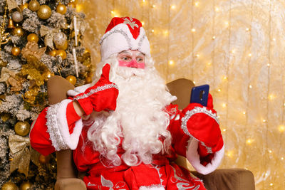Happy santa claus holding smartphone, using mobile app for social communication