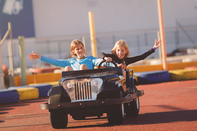 Portrait of girl with sister riding toy car 