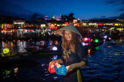 Young woman in hat with gift paper against colored lights