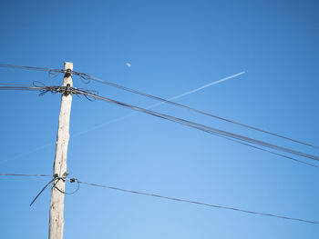 Low angle view of electricity pylon against blue sky