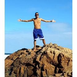 Full length of shirtless man with arms outstretched standing on rock