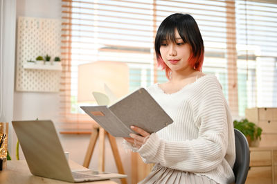 Young woman using digital tablet while sitting on table