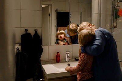 Grandmother brushing teeth of grandson in bathroom at home