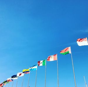 Low angle view of flags hanging against clear blue sky