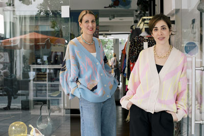 Portrait of female colleagues standing at doorway of clothing store