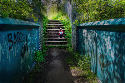 Girl sitting on steps amidst surrounding wall in forest