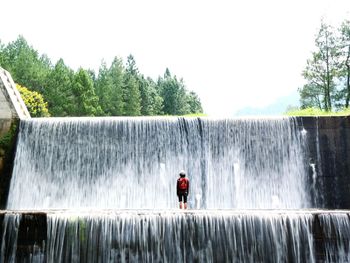 Man standing by waterfall against sky