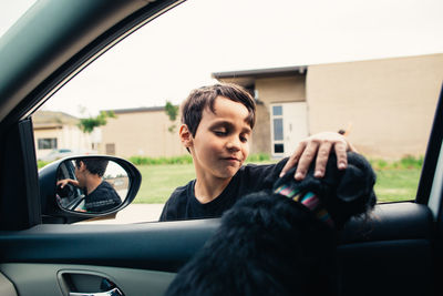 Boy petting dog sitting in car