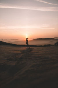 Side view of silhouette woman standing on sand against sky during sunset