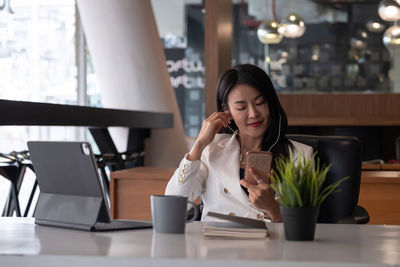 Young woman using mobile phone while sitting on table