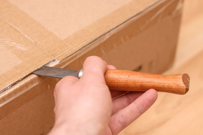 Cropped hand opening cardboard box with knife
