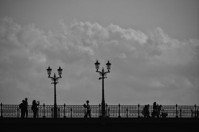 Silhouette people on bridge against sky in city