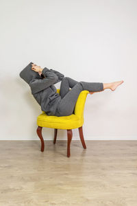 Woman sitting on chair against yellow wall