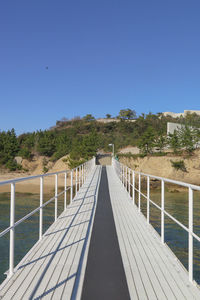 Footbridge on sea against clear blue sky