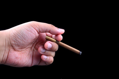 Close-up of hand holding cigarette over black background